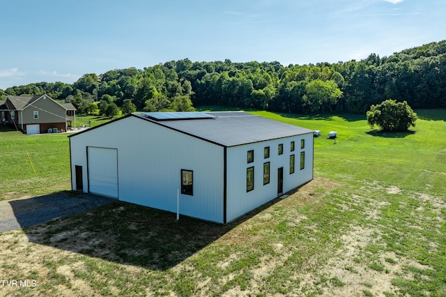 view of pole building with a yard, a forest view, and gravel driveway