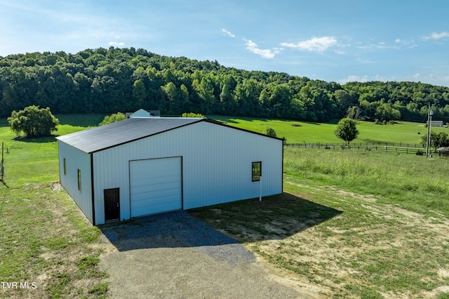 view of outbuilding with a rural view, gravel driveway, fence, an outdoor structure, and a wooded view