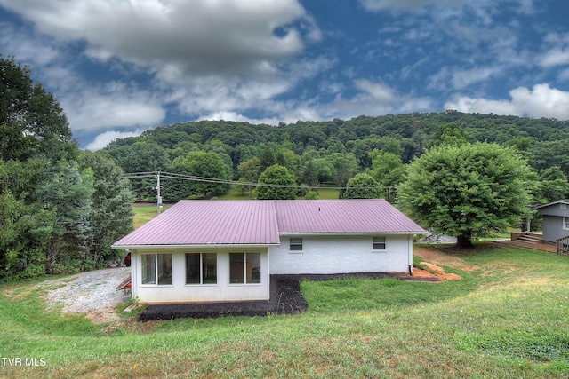 back of house with a forest view, brick siding, metal roof, and a yard