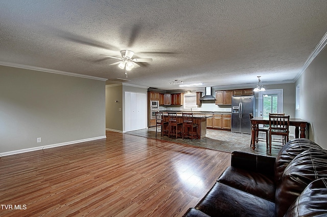 unfurnished living room featuring ceiling fan, a textured ceiling, wood finished floors, baseboards, and ornamental molding