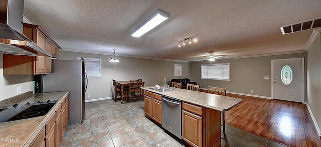 kitchen featuring visible vents, appliances with stainless steel finishes, wall chimney range hood, a center island with sink, and crown molding