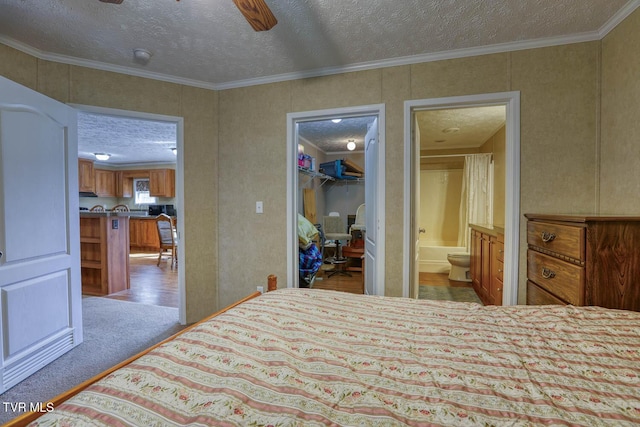bedroom featuring a textured ceiling, carpet floors, a spacious closet, ensuite bath, and crown molding