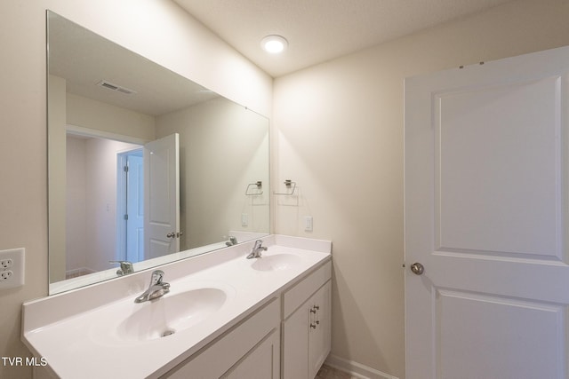 bathroom with double vanity, a sink, visible vents, and baseboards