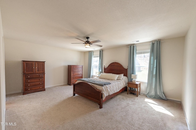 bedroom featuring light carpet, visible vents, baseboards, ceiling fan, and a textured ceiling