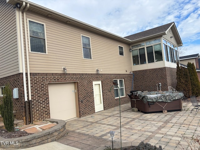 rear view of property with a patio area, brick siding, an attached garage, and a hot tub