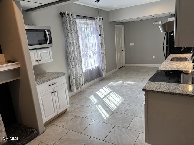 kitchen featuring light stone counters, pendant lighting, stainless steel microwave, white cabinetry, and a sink