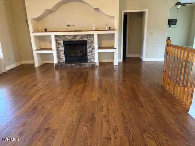 unfurnished living room featuring dark wood-style floors, a fireplace, built in features, and baseboards