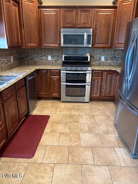 kitchen with stainless steel appliances, light stone countertops, and decorative backsplash