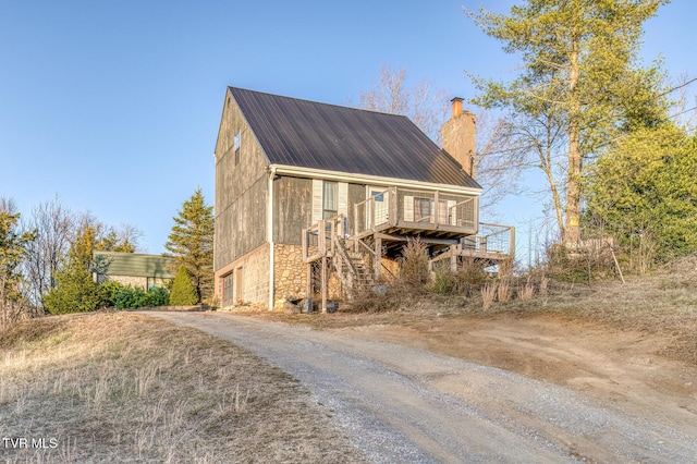 view of front of property with metal roof, driveway, stone siding, stairway, and a chimney