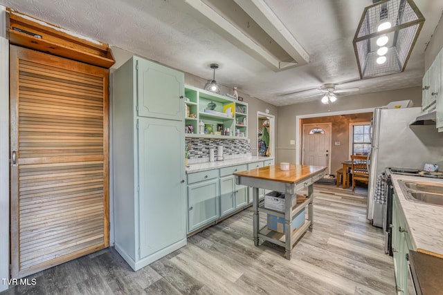 kitchen with open shelves, backsplash, green cabinets, light wood-style floors, and a textured ceiling