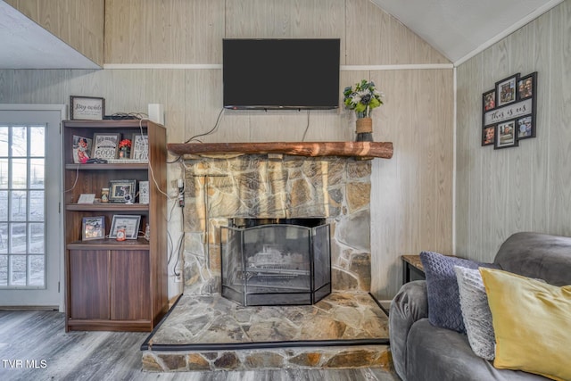 living room featuring vaulted ceiling, wood finished floors, and a stone fireplace