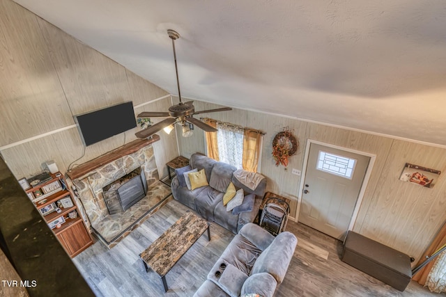 living room with vaulted ceiling, a stone fireplace, wood finished floors, and a wealth of natural light