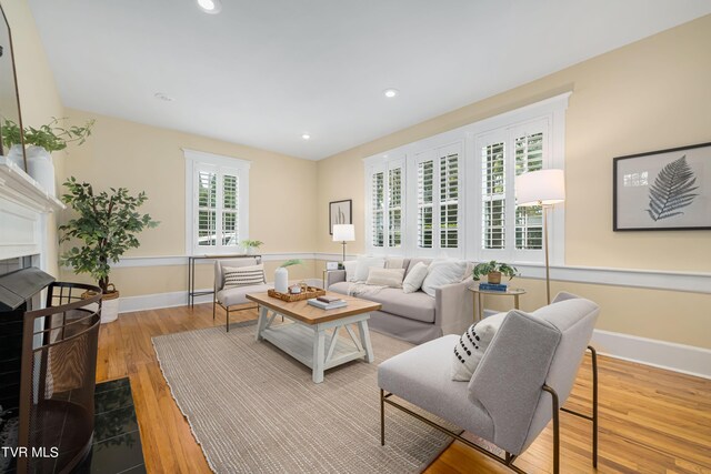 living area with wood finished floors, recessed lighting, a fireplace with flush hearth, and baseboards