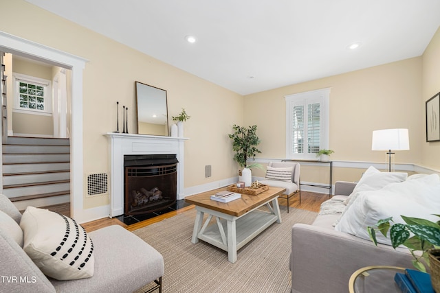 living area featuring stairs, a wealth of natural light, a fireplace, and wood finished floors