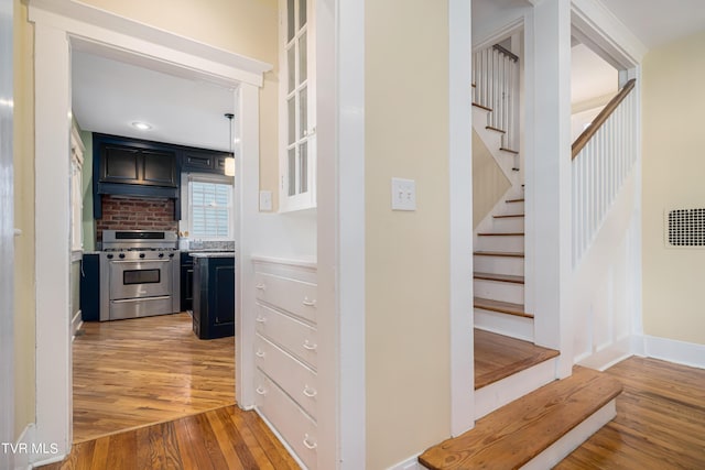 hallway with stairs, light wood finished floors, and visible vents