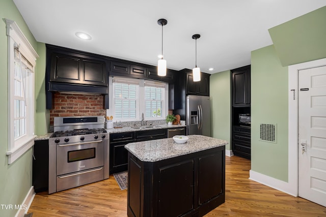 kitchen featuring light wood-style flooring, a kitchen island, stainless steel appliances, dark cabinetry, and a sink