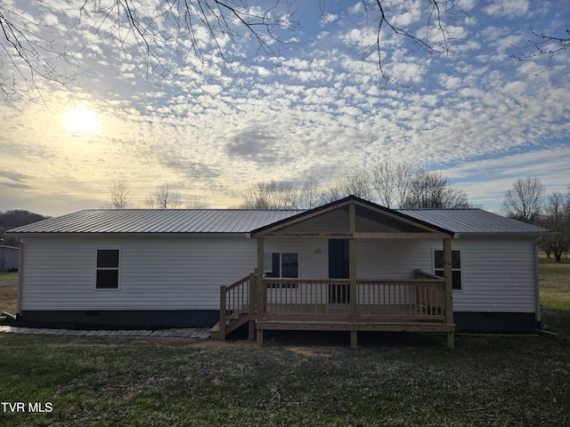 rear view of property featuring crawl space, a deck, metal roof, and a lawn