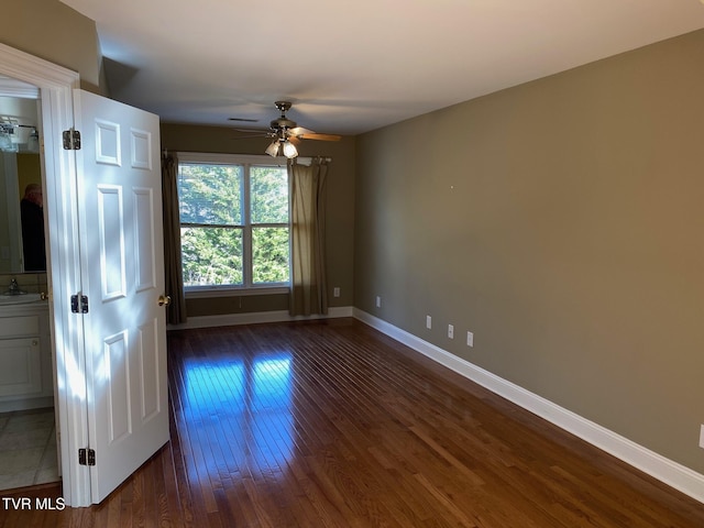 interior space with a ceiling fan, a sink, dark wood finished floors, and baseboards