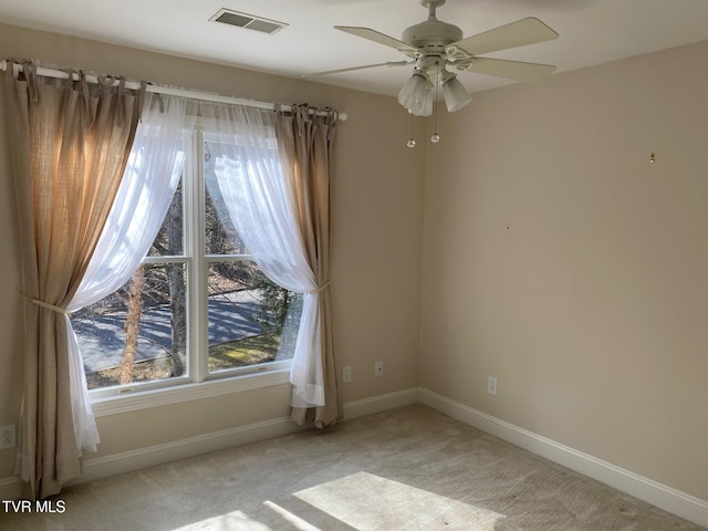 empty room featuring a ceiling fan, light colored carpet, visible vents, and baseboards