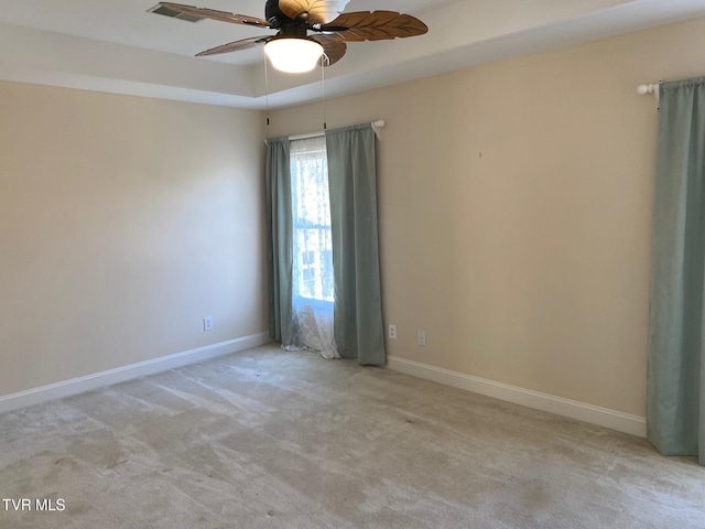 carpeted empty room with a ceiling fan, a raised ceiling, and baseboards