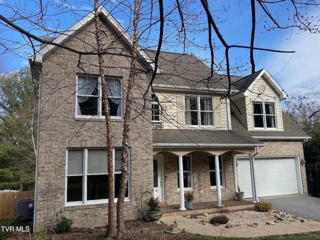 traditional home featuring a shingled roof, brick siding, fence, and aphalt driveway