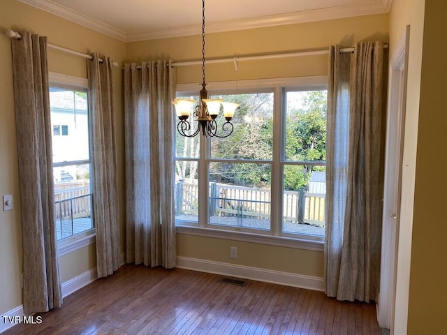 unfurnished dining area with visible vents, baseboards, hardwood / wood-style floors, an inviting chandelier, and crown molding