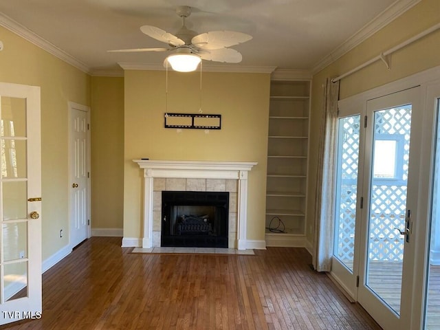 unfurnished living room with baseboards, a tiled fireplace, wood-type flooring, ornamental molding, and built in shelves