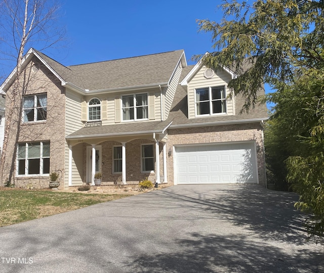 traditional-style home with a garage, a shingled roof, aphalt driveway, and brick siding