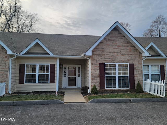 view of front facade featuring stone siding, a shingled roof, and fence