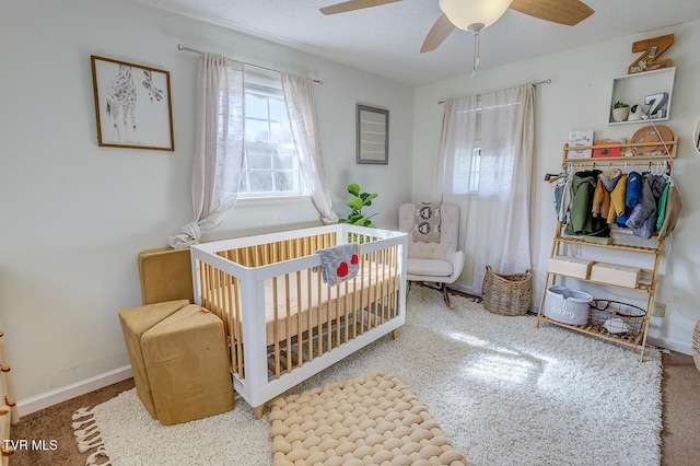 bedroom featuring ceiling fan, a crib, and baseboards