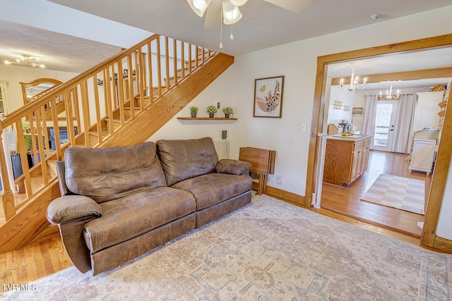 living room with ceiling fan with notable chandelier, baseboards, light wood finished floors, and stairs