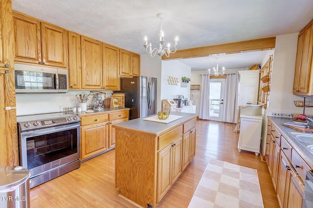 kitchen with decorative light fixtures, a notable chandelier, light wood finished floors, stainless steel appliances, and a kitchen island