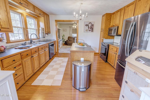 kitchen with light wood finished floors, a center island, stainless steel appliances, a chandelier, and a sink