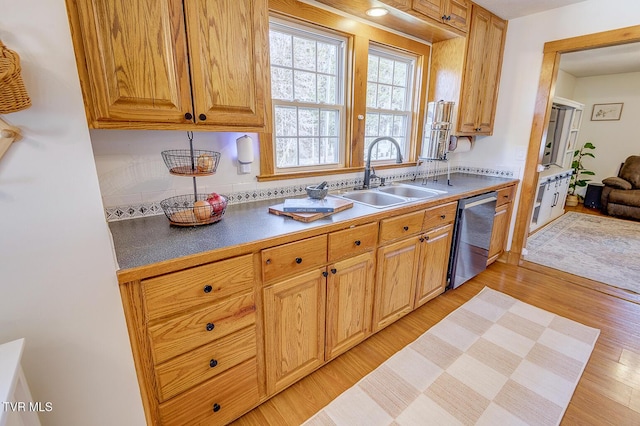 kitchen with light wood finished floors, decorative backsplash, dark countertops, a sink, and stainless steel dishwasher