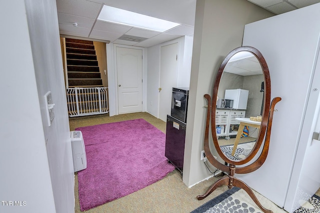 hallway featuring a paneled ceiling, carpet, and stairs