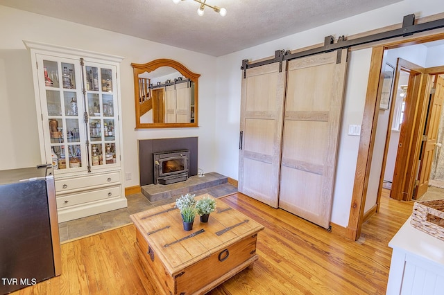 living area with a textured ceiling, a barn door, light wood-style flooring, and baseboards