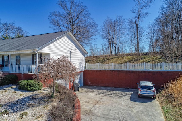 view of property exterior featuring a garage, covered porch, fence, and concrete driveway