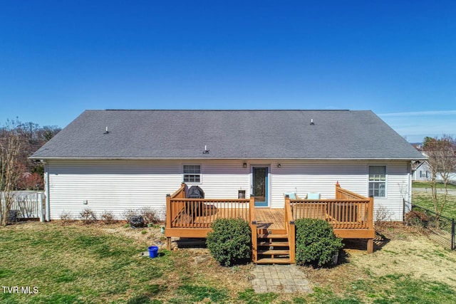 back of property with a shingled roof, fence, a wooden deck, and a lawn