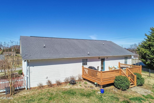 rear view of house featuring a shingled roof, fence, and a wooden deck