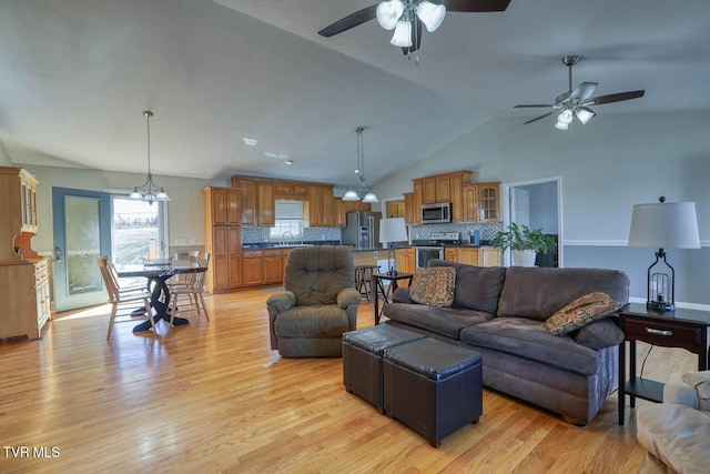 living area with lofted ceiling, light wood finished floors, and ceiling fan with notable chandelier