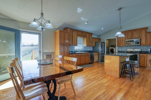 kitchen featuring dark countertops, lofted ceiling, light wood-style flooring, appliances with stainless steel finishes, and washer / dryer