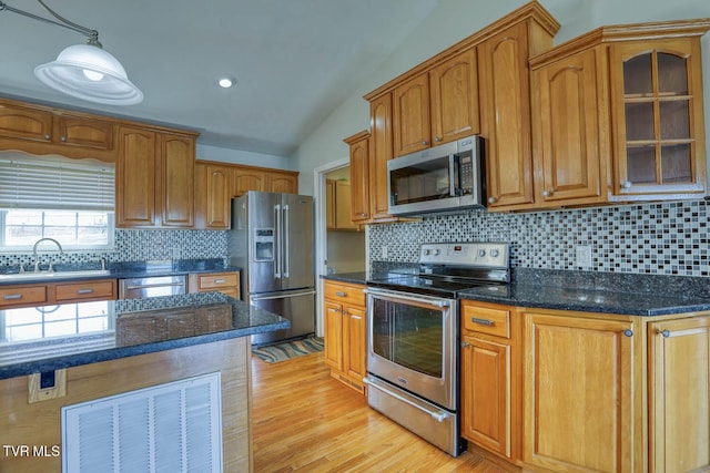 kitchen with lofted ceiling, stainless steel appliances, a sink, light wood-type flooring, and dark stone counters