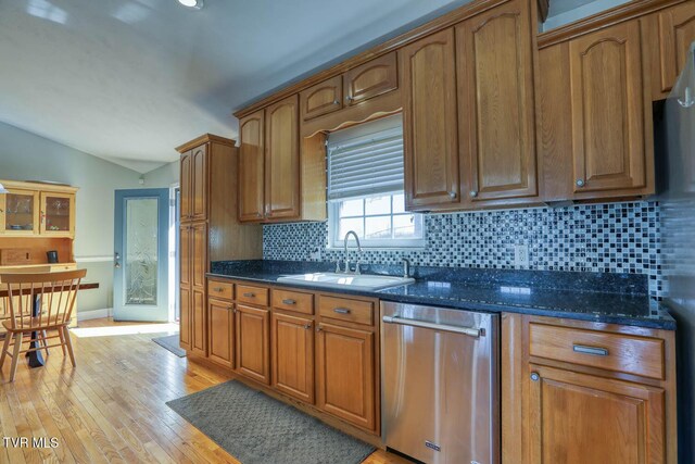 kitchen featuring light wood-style flooring, a sink, vaulted ceiling, stainless steel dishwasher, and backsplash