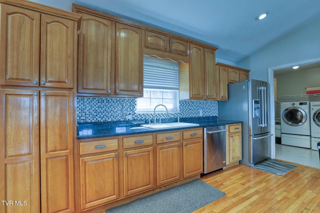 kitchen featuring decorative backsplash, appliances with stainless steel finishes, dark stone countertops, washing machine and clothes dryer, and a sink