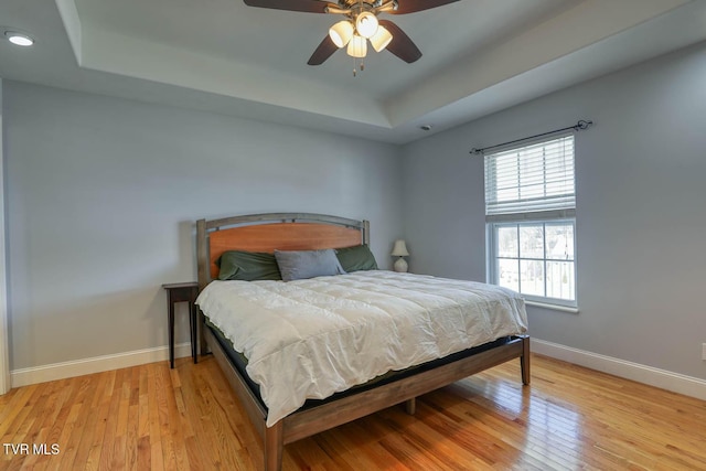 bedroom featuring light wood finished floors, ceiling fan, a tray ceiling, and baseboards