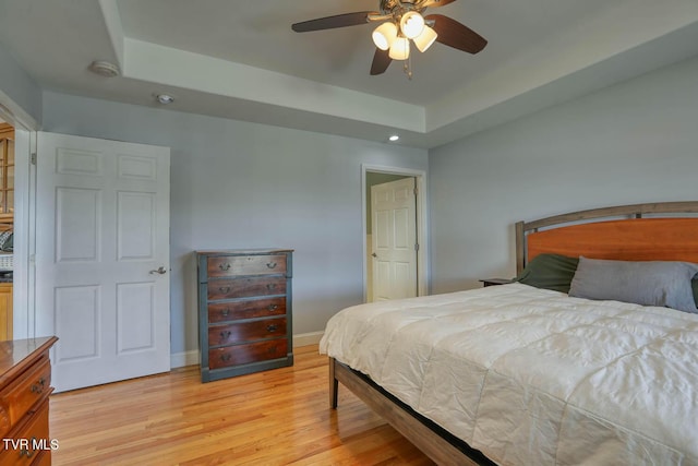 bedroom with light wood-style floors, baseboards, a tray ceiling, and recessed lighting