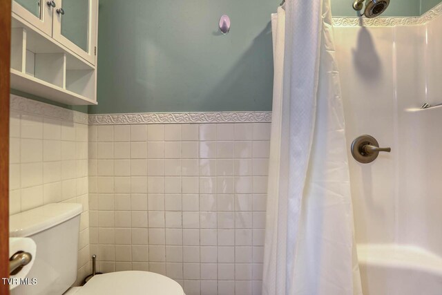 full bathroom featuring toilet, a wainscoted wall, and tile walls