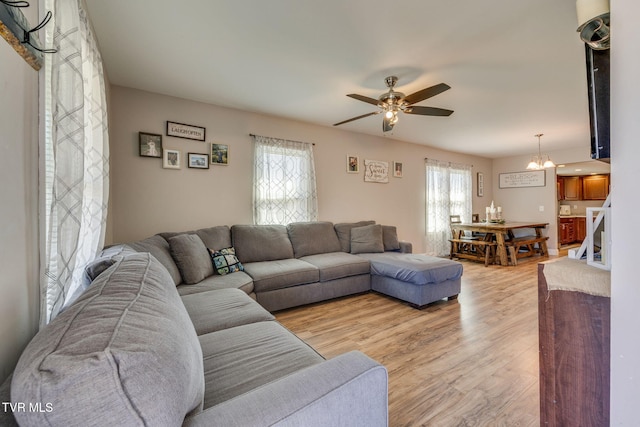 living area featuring light wood-style flooring and ceiling fan with notable chandelier