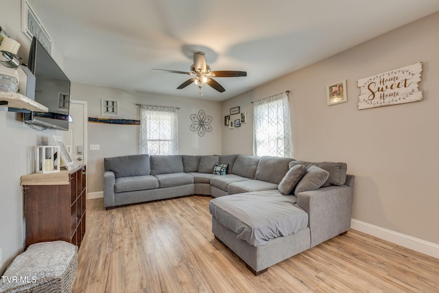 living area with light wood-type flooring, a ceiling fan, baseboards, and a wealth of natural light