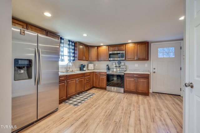 kitchen featuring recessed lighting, light wood-style flooring, appliances with stainless steel finishes, brown cabinetry, and a sink